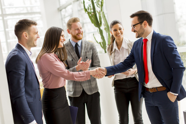 Business partners handshaking after making agreement with employees near by